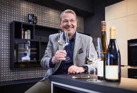 Foto eines lächelnden Mannes mit Weinglas in der Hand.