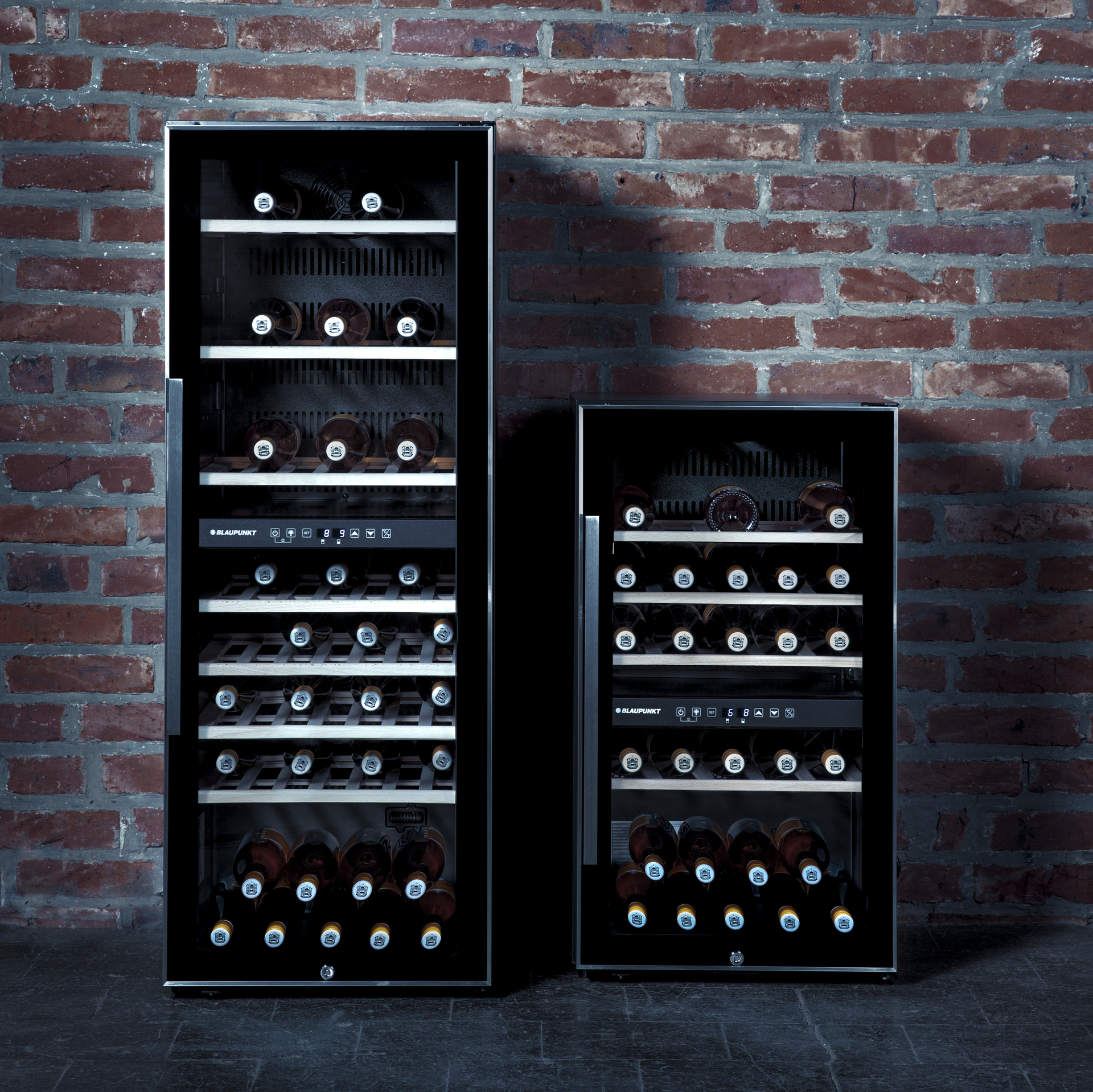 Dos vinotecas independientes de la marca Blaupunkt, de dos tamaños diferentes y con puerta de cristal, situadas frente a una pared de ladrillo