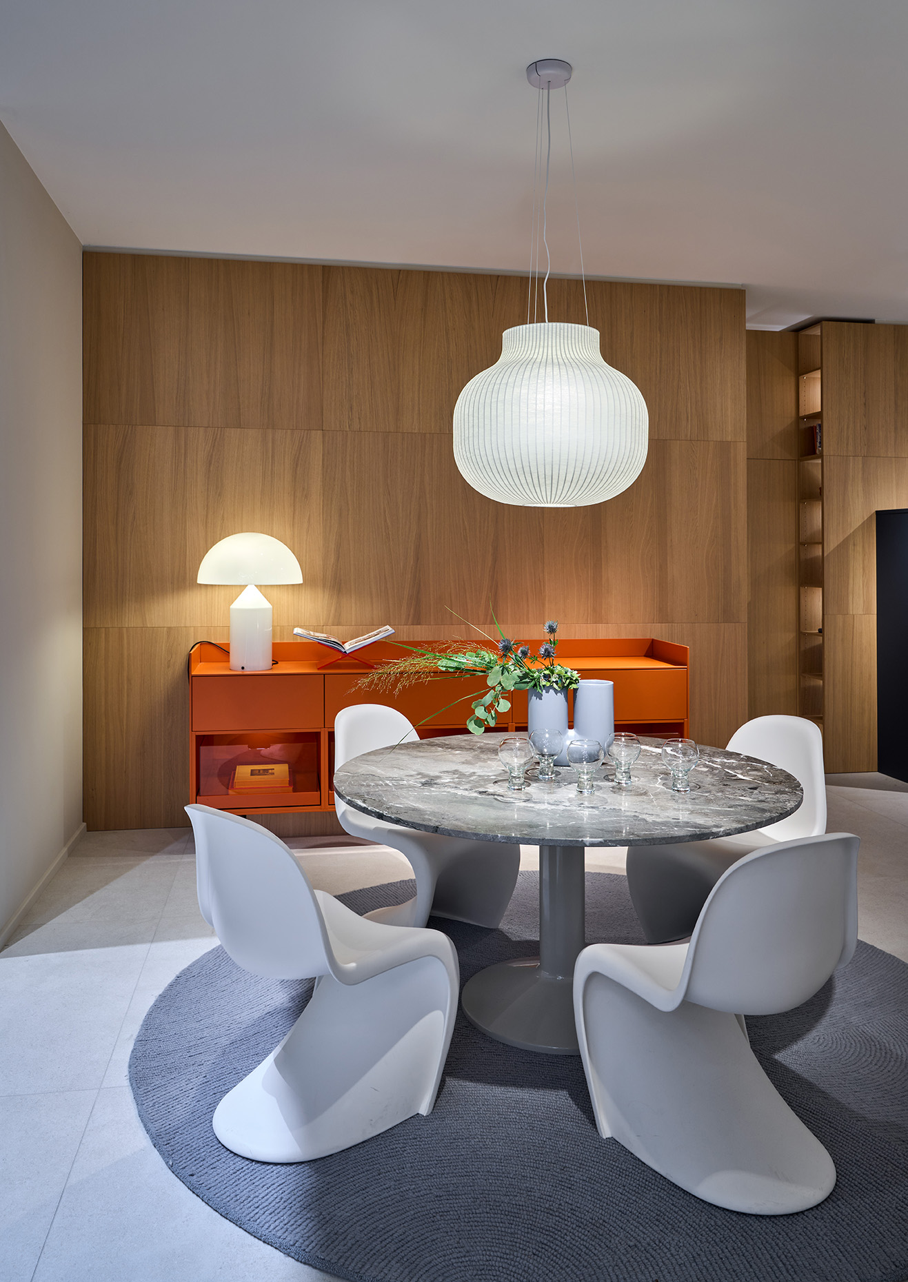 Round dining table with designer chairs and an orange sideboard with a designer lamp