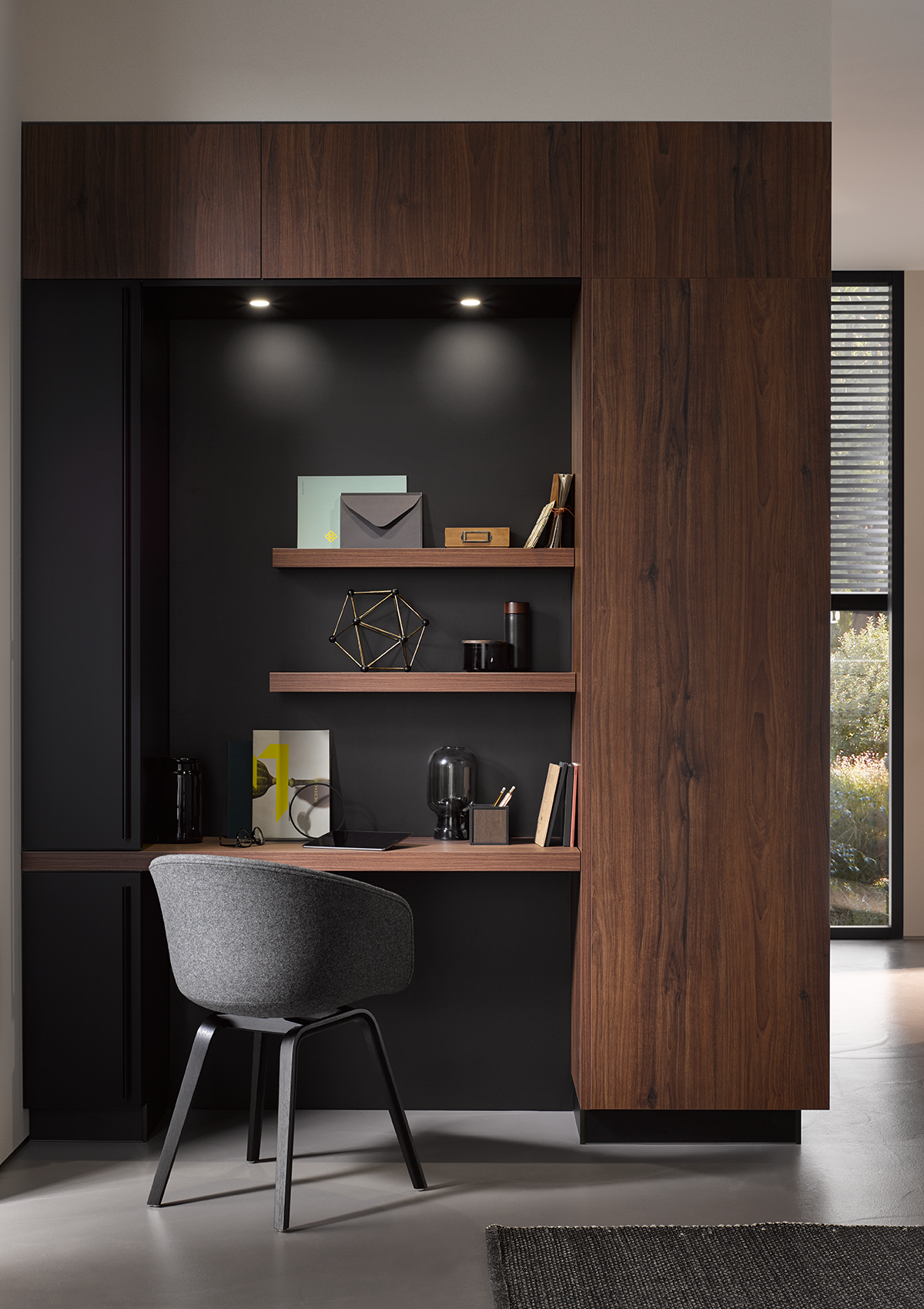 Arbeitsnische mit schwarzer Rückwand, Nussbaum-Tischplatte sowie passenden Regalen und integrierten Lichtspots.