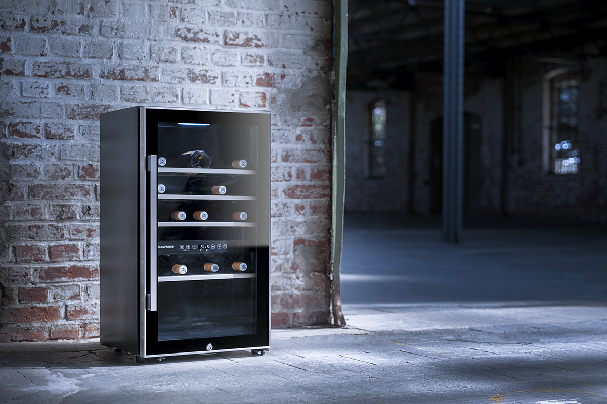Nevera para vinos Blaupunkt compacta e independiente, con puerta de cristal, situada junto a una pared de ladrillo en un loft